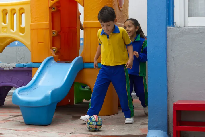 Niña y niño jugando futbol en el patio de Happy Days